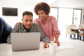 Middle aged black mum helping her teenage son do his homework using a laptop, close up