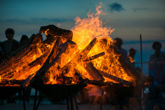 Large burning bonfire with soft glowing flame and sparkles flying all around. Romantic summer evening, people relaxing and enjoying calmness at the seaside during the Night of ancient lights.  