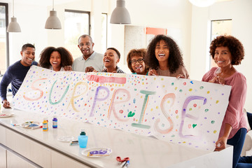 Three generation black family holding up a sign theyâ€™ve made for a surprise party at home