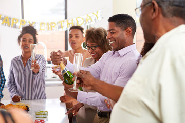 Middle aged black man opening champagne to celebrate with his three generation family, close up
