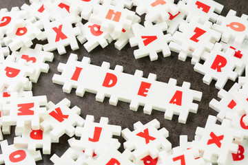 Idea, creativity or business solution concept, white puzzle jigsaw with alphabet building the word Idea at the center of dark chalkboard