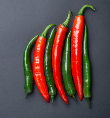 Green and red chili peppers on black background, top view. Hot spicy food symbol.