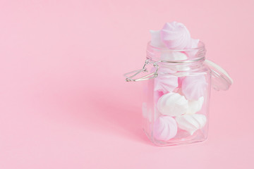 White and pink twisted meringues in a glass jar on pink background. French dessert prepared from whipped with sugar and baked egg whites. Greeting card with copy space