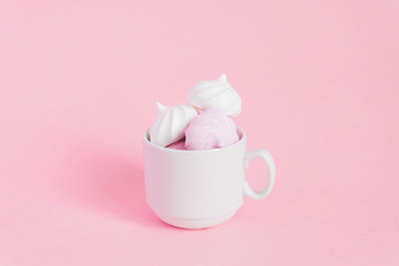 White and pink twisted meringues in a small porcelain coffe cup on pink background. French dessert prepared from whipped with sugar and baked egg whites. Greeting card with copy space