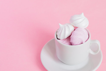 White and pink twisted meringues in a small porcelain coffe cup on pink background. French dessert prepared from whipped with sugar and baked egg whites. Greeting card with copy space