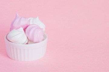 white and pink twisted meringues in porcelain bowl on pink background, greeting card, copy space