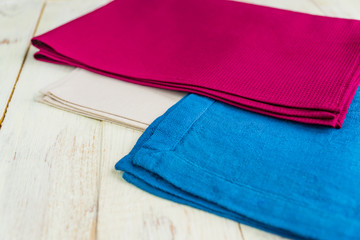 close up of cloth napkins of beige, blue and burgundy colors on rustic white wooden table. Shallow depth of field.