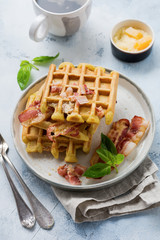 Cheese Waffles with fried bacon, egg and parmesan cheese with spices and basil for breakfast on light old concrete background. Top view.