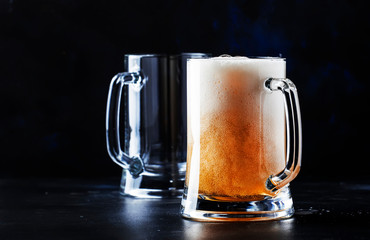 Two glasses of german light beer, beer poured into mug, dark bar counter, selective focus