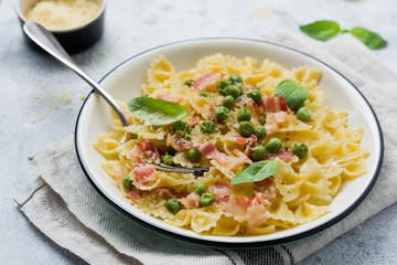 Fettuccine pasta with bacon and green peas and parmesan cheese in light plate on old gray concrete background. Top view.
