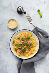 Fettuccine pasta with bacon and green peas and parmesan cheese in light plate on old gray concrete background. Top view.