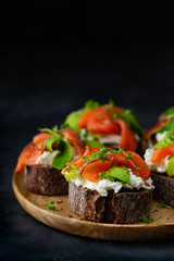 Homemade toast sandwich with rye bread, salmon, avocado, cottage cheese and microgreen sprouts on dark board background. healthy food - breakfast close-up