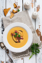 Potato soup cream with bacon and soy sauce in white bowl, on light old wooden background. Top view.