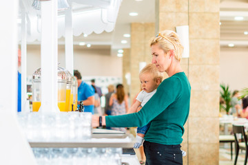 Mother with baby boy enjoying orange juice in all inclusive restaurant