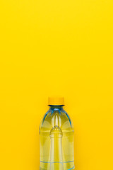 minimalist photo of plastic water bottle with yellow cap on the yellow background with copy space