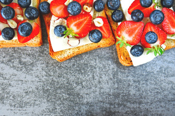 Healthy toasts with white cheese, fresh strawberries and blueberries. The concept of a healthy snack or lunch. 