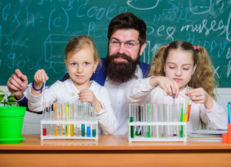 School time. Schoolgirls holding test tubes guided by teacher. School children performing experiment in science classroom. Science laboratory for school and education. Laboratory in elementary school