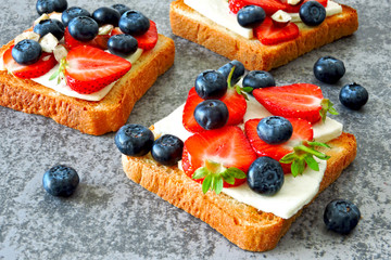 Healthy toasts with white cheese, fresh strawberries and blueberries. The concept of a healthy snack or lunch. 