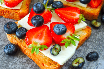 Healthy toasts with white cheese, fresh strawberries and blueberries. The concept of a healthy snack or lunch. 