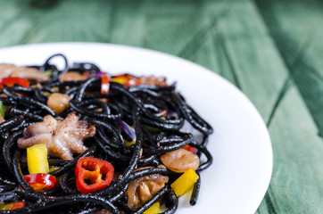 black spaghetti with seafood and vegetables on a green background of Kopi space