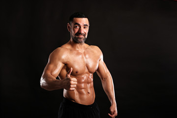 Fototapeta na wymiar Portrait of young handsome muscular bodybuilder on black background showing big finger up , like 