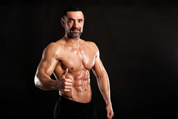 Fototapeta premium Portrait of young handsome muscular bodybuilder on black background showing big finger up , like 