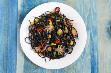 black spaghetti with seafood and vegetables on blue background close-up top view