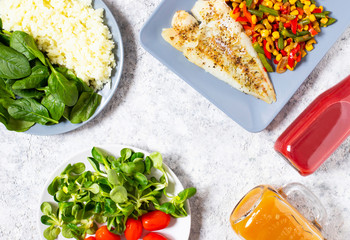 Healthy lunch. The concept of healthy eating. Baked fish, rice, fresh spinach, lettuce, cherry tomatoes, baked fresh vegetables, a bottle of grapefruit fresh and a bottle of cherry and apple fresh