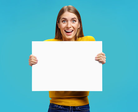 Happy girl with white empty poster on blue background. Copy space for your text.