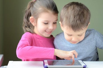 White caucasian toddler boy and beautiful girl playing together on tablet games. Portrait of a happiness little brother and sister. Children play a computer game on the tablet