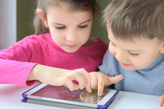 White caucasian toddler boy and beautiful girl playing together on tablet games. Portrait of a happiness little brother and sister. Children play a computer game on the tablet