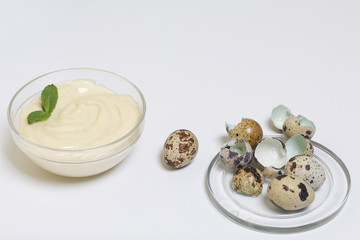 Handmade mayonnaise using quail eggs. In a glass container, decorated with greenery. Near quail eggs and shell from them. On a white background.