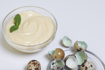 Handmade mayonnaise using quail eggs. In a glass container, decorated with greenery. Near quail eggs and shell from them. On a white background.
