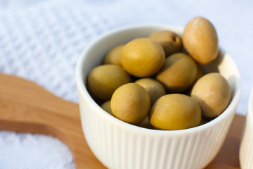 set of three white bowls with olives on wooden tray on white blanket