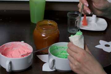 Woman fills a pastry bag with cream. Cream of different colors for decorating cake Basket. Nearby is a jar of jam.