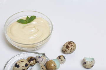 Handmade mayonnaise using quail eggs. In a glass container, decorated with greenery. Near quail eggs and shell from them. On a white background.