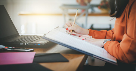 Closeup of hand asian businesswoman writing on document and working with laptop in office