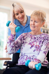 Female Physiotherapist Helping Senior Woman In Wheelchair To Lift Hand Weights