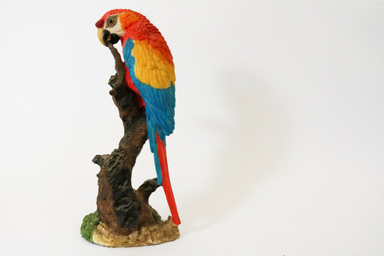 Statuetta di un pappagallo colorato appoggiato su un ramo,sfondo bianco