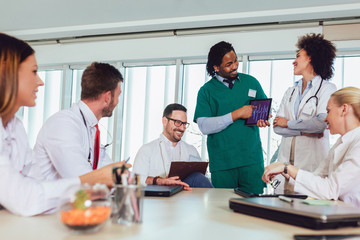 Medical team sitting and discussing at the table in the office, using digital tablet.