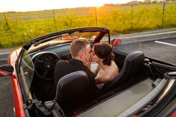 Beautiful wedding couple watching the sunset in a convertible car.