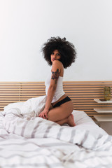 Fototapeta na wymiar Young charming black woman in lingerie posing on bed