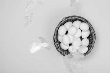 White Eggs in a Wicker Basket with Feathers on Textured Paper Background. One of the Easter Symbols. Some Feathers is Specially in Blurred Focus. Black and White Vintage Photo.