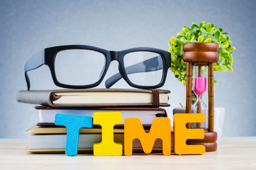 Time management concept, hourglass and spectacles on wooden desk over dark background