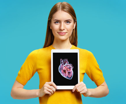 Girl shows the x-ray image of the heart. Photo of young girl with tablet in her hands on blue background. Medical concept
