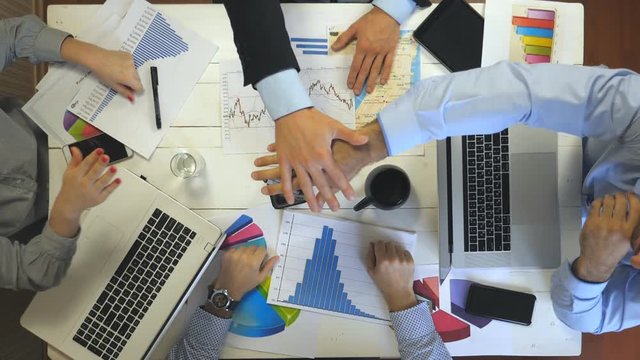 Top view to hands of four business people celebrating achievement. Group of employers stacked arms together one by one in unity showing joyful. Creative team working at modern office. Success concept