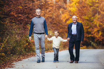Elderly father adult son and grandson out for a walk in the park.