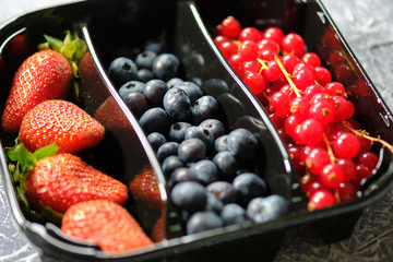 plastic containers box of berries, red currants, blueberries, and strawberries on the grey background