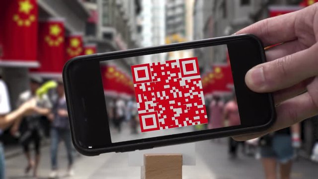 Scanning QR CODE look alike pattern (CAN NOT SCAN THIS) to make a cashless payment via smart phone.  Blurred street in China background.