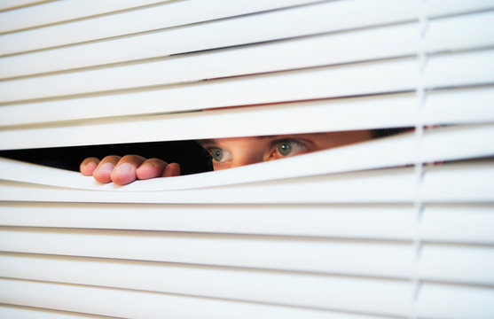A man looking through slats of blinds